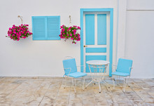 Classic View Of A Greek Blue Window On A White Wall With Coffee Table And Chairs On The Cyclades