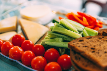 Close-up buffet of cherry tomatoes, cucumbers, cheese and slices of black bread on the table. Soft focused picture. Snack before dinner. A healthy and balanced diet. Light breakfast. Good morning