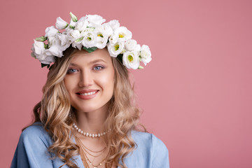 Spring beauty studio portrait of young beautiful happy smiling blonde woman with natural makeup, long waved hair, wearing flower wreath, posing on pink background, Copy, empty space for text