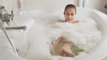 Close-up Of A Pretty Little Girl Squishes Feet In A Bathtub Full Of Foam. Hygiene And Baby Care Concept, HD Still Video Camera, 4x Slow Motion.