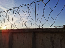 Prison Walls With Barbed Wire On A Sunset Background. Concrete Fence With Barbed Wire.