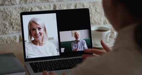 Wall Mural - Young woman daughter video calling senior old parents by web cam having distance online conversation, virtual conference chat using videocall application on laptop. Over shoulder closeup screen view.