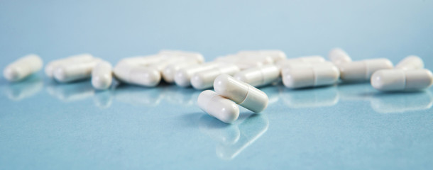 Two white capsules and heap of capsules on blue background. High resolution product. Health care concept