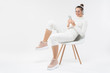 © Damir Khabirov - Young smiling woman sitting on white chair, listening to music in wireless headphones, chatting on phone with friends, isolated on gray background