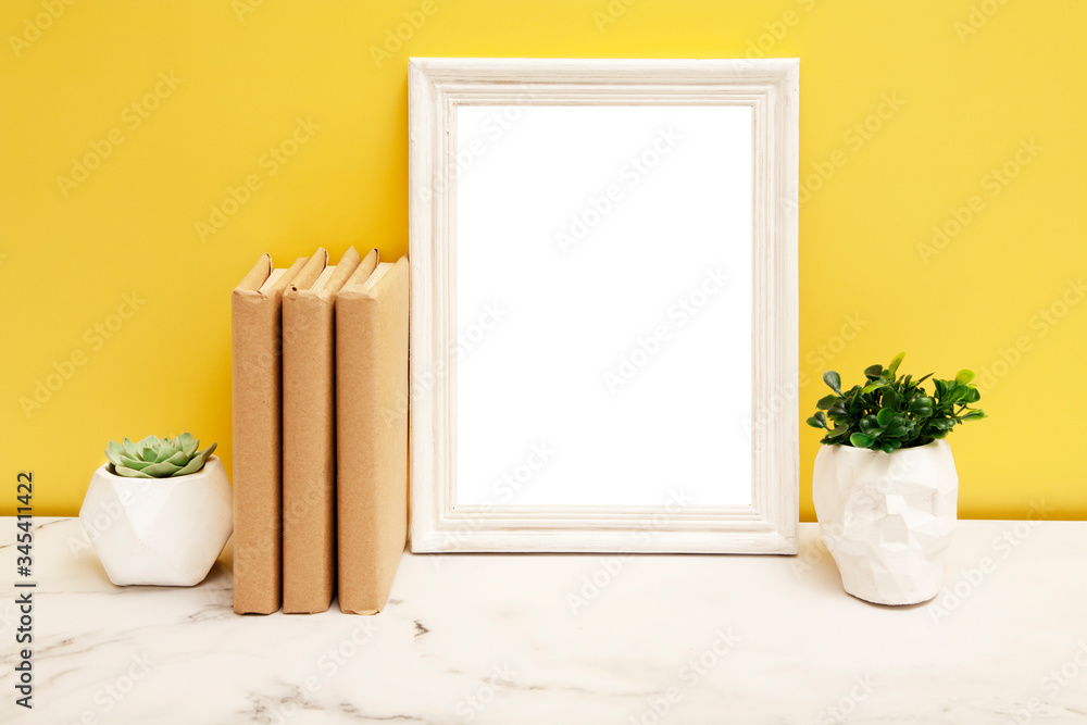 Empty white frame mock-up with a home plants and books on the table on yellow background - obrazy, fototapety, plakaty 