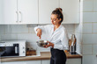 © Daria - Beautiful, attractive, smiling young woman kneading dough with whisk for banana pancakes in steel dishes in a kitchen with white, light interior. Monochrome photo without bright accents