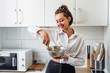 © Daria - Beautiful, attractive, smiling young woman kneading dough with whisk for banana pancakes in steel dishes in a kitchen with white, light interior. Monochrome photo without bright accents