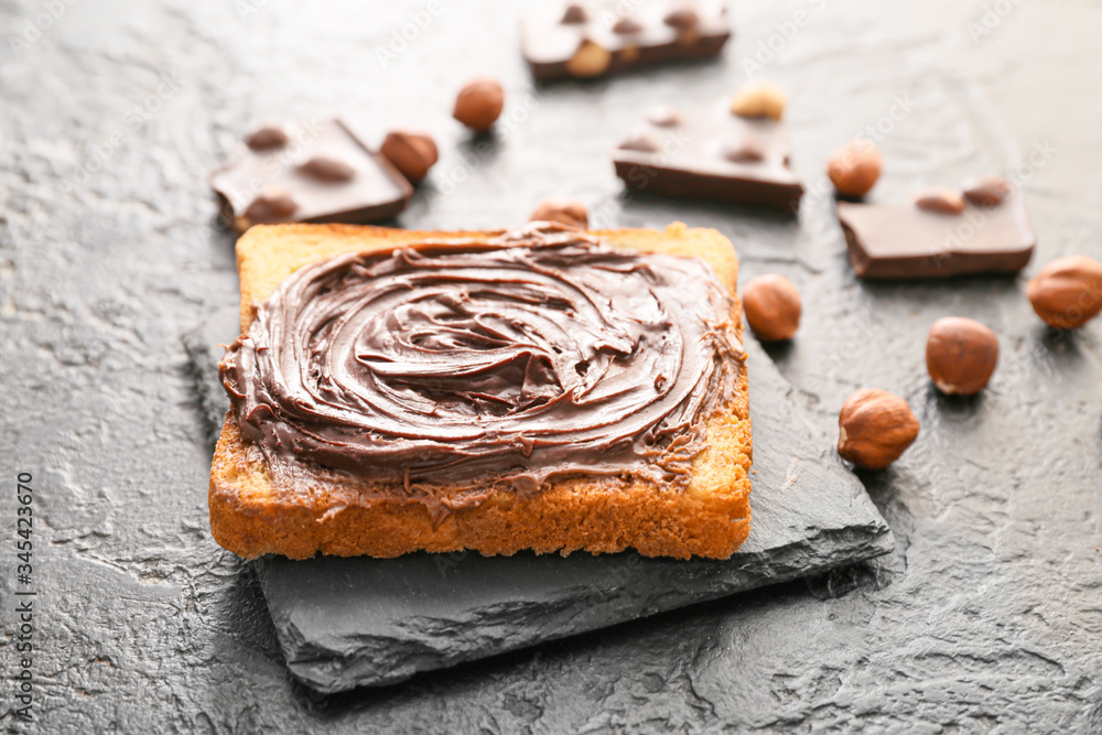 Fresh bread with chocolate paste and hazelnuts on dark background
