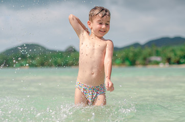 
happy child splashes on the ocean. The kid smiles and bathes in the sea. Beautiful coast of the ocean, a child is played on the seashore. Boy at the sea.
