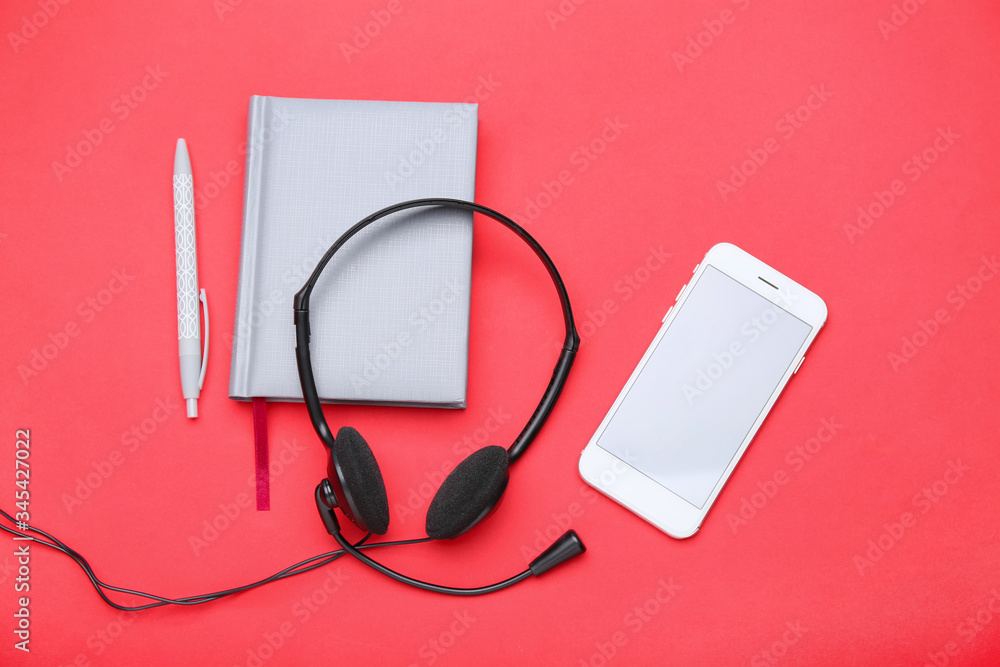 Mobile phone with headset and notebook on color background