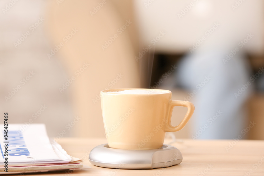 Cup of coffee with heater and newspaper on table