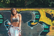 Relaxed Young Confident Stylish Woman Tying Shirt Around Waist On Graffiti Wall Background