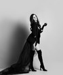 © Dmitry Lobanov - Young beautiful brunette woman in black clothes with long transparent hem and high boots making step and looking at camera