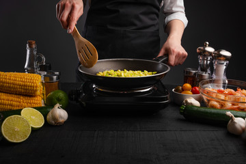 Wall Mural - Chef fries vegetables, with space on a black wooden table. Culinary and gastronomy. Book of culinary recipes.
