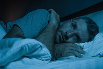 dramatic portrait in the dark of attractive depressed and worried man on bed suffering depression crisis and anxiety feeling lost lying sleepless in insomnia and life problem concept