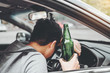 © joyfotoliakid - Drunk man driving a car on the road holding bottle beer Dangerous drunk driving concept
