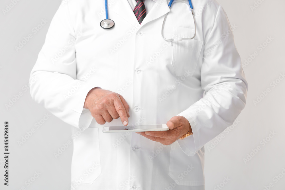 Mature male doctor with tablet computer on grey background