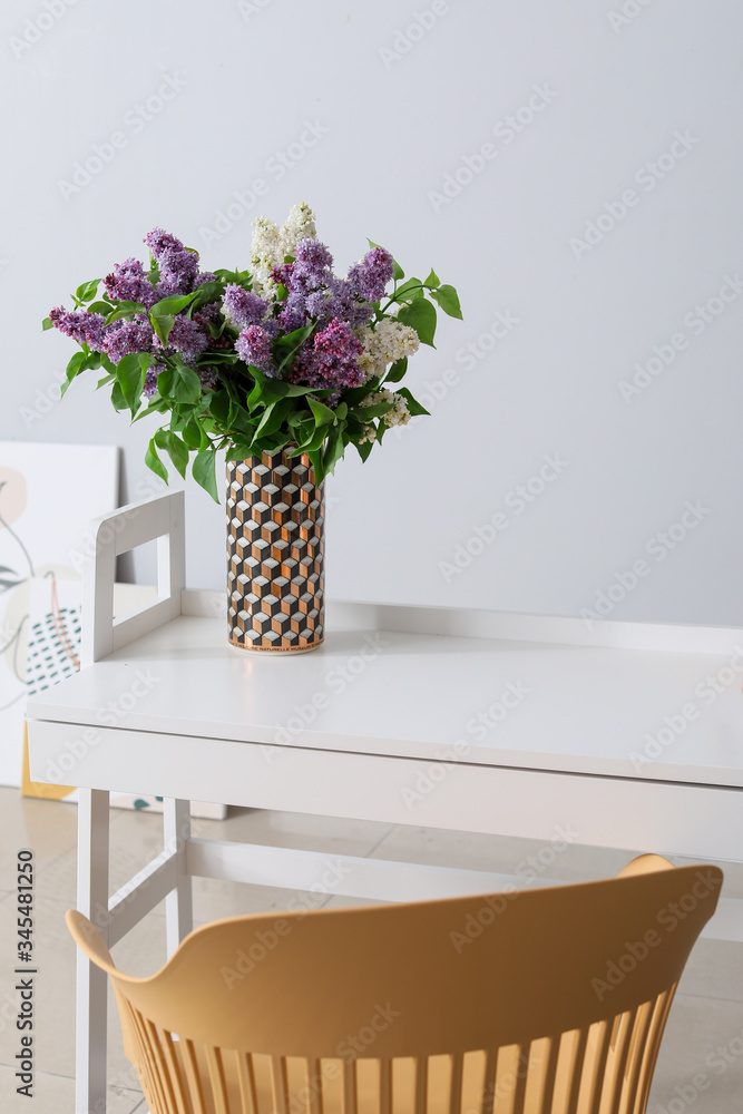 Beautiful lilac flowers on table near grey wall in room