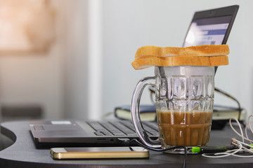 two bread put on top of hot coffee cup and smart phone, laptop on black table for work from home