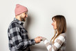 © Alex - Young man with a beard in a hat and a plaid shirt and a girl in a sweater hold hands on an isolated light background. Emotional face. Happy couple dating