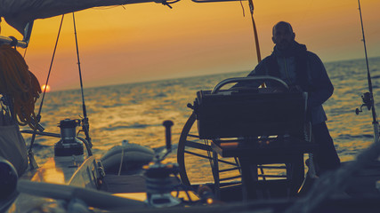 Wall Mural - Sailor steering sailing boat with a rudder in dawn / twilight time on tje open sea.