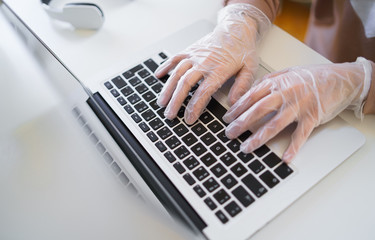 Wall Mural - Unrecognizable woman with gloves at the table, using laptop in quarantine.