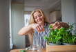 © Halfpoint - Front view portrait of woman indoors at home, cutting herbs.