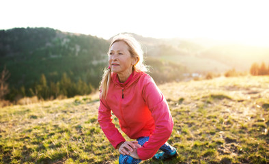 Wall Mural - Attractive senior woman doing exercise outdoors in nature at sunset.