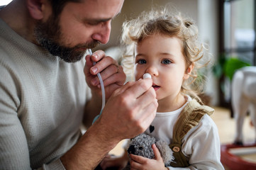 Wall Mural - Father with small sick daughter indoors at home, using nasal aspirator.