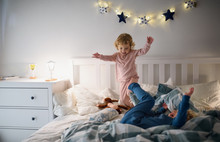 Two Small Children Jumping On Bed Indoors At Home, Having Fun.