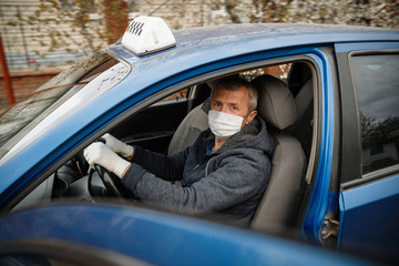 A man driving a car in a protective medical mask and gloves. Safe drive in a taxi during a pandemic coronavirus. Protect the driver and passengers from bacteria and virus infection in quarantine