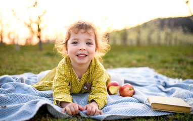 Small toddler girl sitting outdoors on blanket in spring, looking at camera.