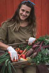 Portrait of a young dark woman with vegetables on the background of a red wooden house