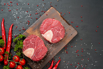 Wall Mural - Two raw fresh marbled meat steak on dark background, cherry tomatoes and spices. Close up.