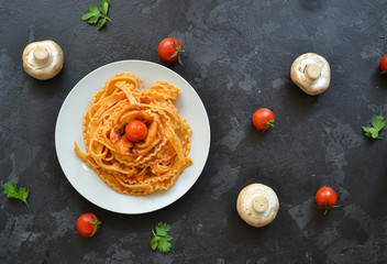 Pasta in a white plate. Pasta with tomato sauce, mushrooms with cherry tomatoes. Dark background. View from above. Free space for text. One plate