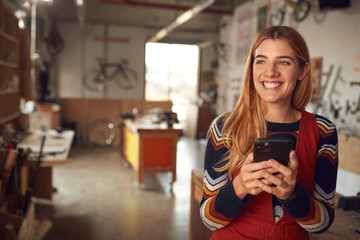 Female Business Owner In Workshop Using Mobile Phone