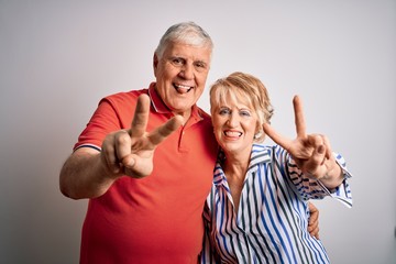 Wall Mural - Senior beautiful couple standing together over isolated white background smiling with tongue out showing fingers of both hands doing victory sign. Number two.