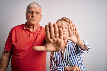 Wall Mural - Senior beautiful couple standing together over isolated white background doing stop sing with palm of the hand. Warning expression with negative and serious gesture on the face.