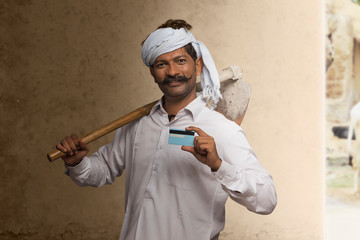 Portrait of Indian rural farmer holding credit card and carrying hoe on his shoulder
