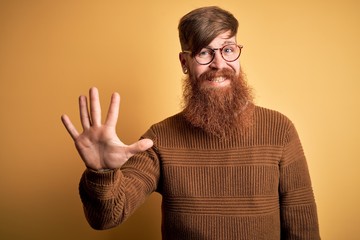 Canvas Print - Handsome Irish redhead man with beard wearing glasses and winter sweater over yellow background showing and pointing up with fingers number five while smiling confident and happy.