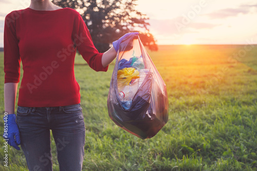 young volunteer woman collecting trash at sunset or sunrise light, earth nature  plastic pollution concept
