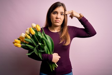 Sticker - Young blonde woman holding romantic bouquet of yellow tulips flowers over pink background Shooting and killing oneself pointing hand and fingers to head like gun, suicide gesture.