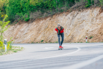 Wall Mural - Tall fit male longboarder riding his longboard downhill on a sunny day high in nature while wearing a red shirt, green hat, and grey jeans.