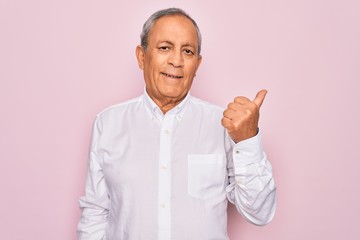 Sticker - Senior handsome grey-haired man wearing elegant shirt over isolated pink background smiling with happy face looking and pointing to the side with thumb up.