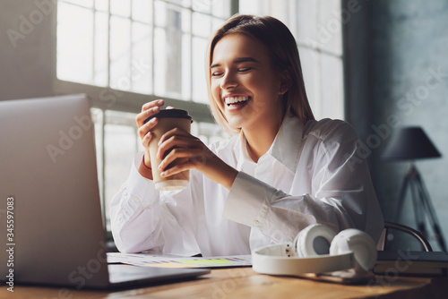 Fotomural Smiling girl sits at table in front of laptop and study remotely