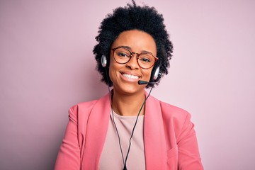 Wall Mural - Young African American call center operator woman with curly hair using headset happy face smiling with crossed arms looking at the camera. Positive person.