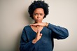 Young beautiful African American afro woman with curly hair wearing casual sweater Doing time out gesture with hands, frustrated and serious face