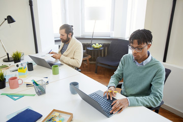 Wall Mural - horizontal high angle shot of two modern white collar workers sitting at tables doing their job usin
