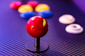 Red joystick and colorful buttons of vintage arcade game console. Close up view of old game control panel. Red sphere, ball. 