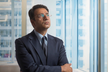 Wall Mural - Businessman in formal clothes and eyeglasses thinking deeply looking away with arms crossed
